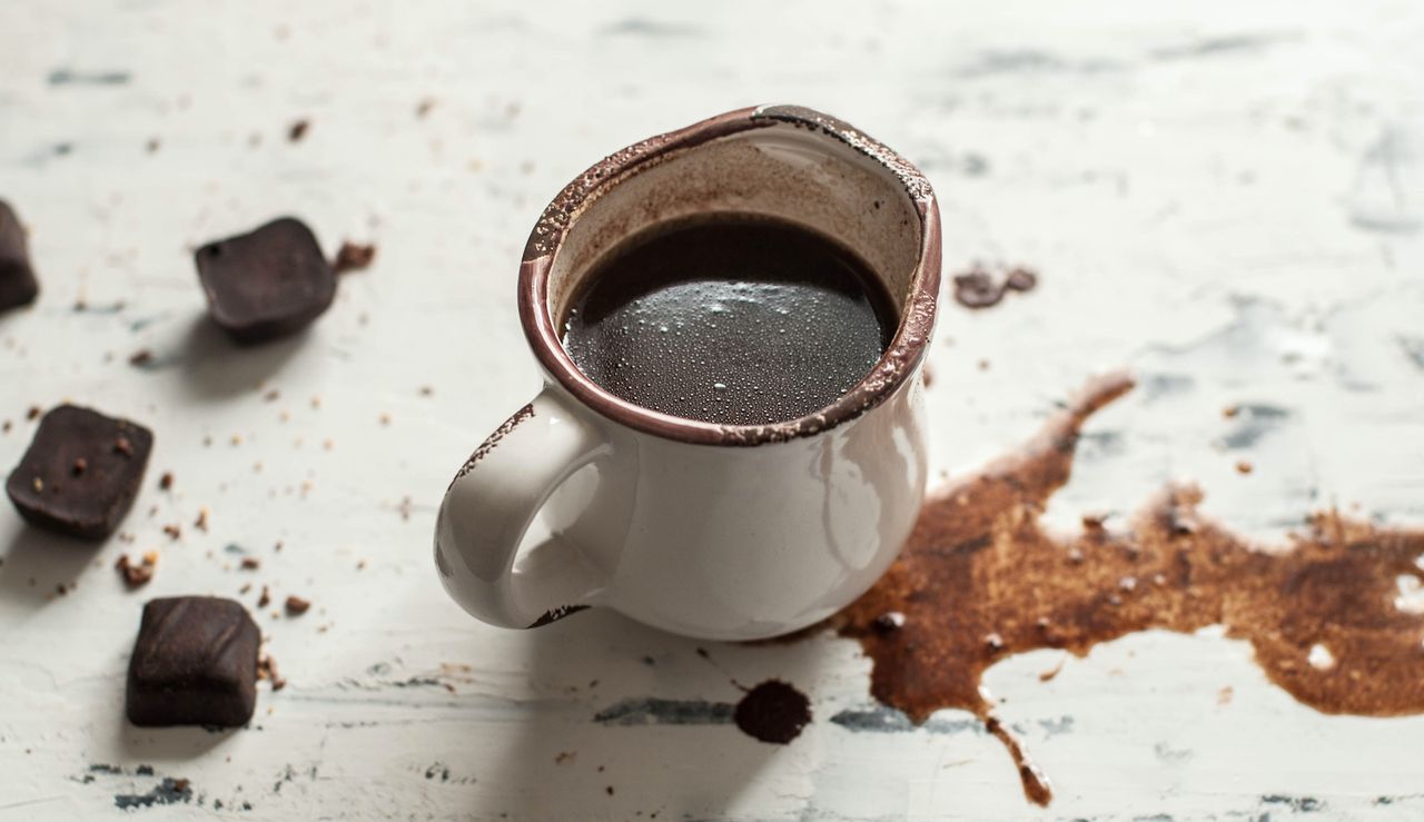 hot chocolate spilled on a white rustic table with edible chocolates nearby