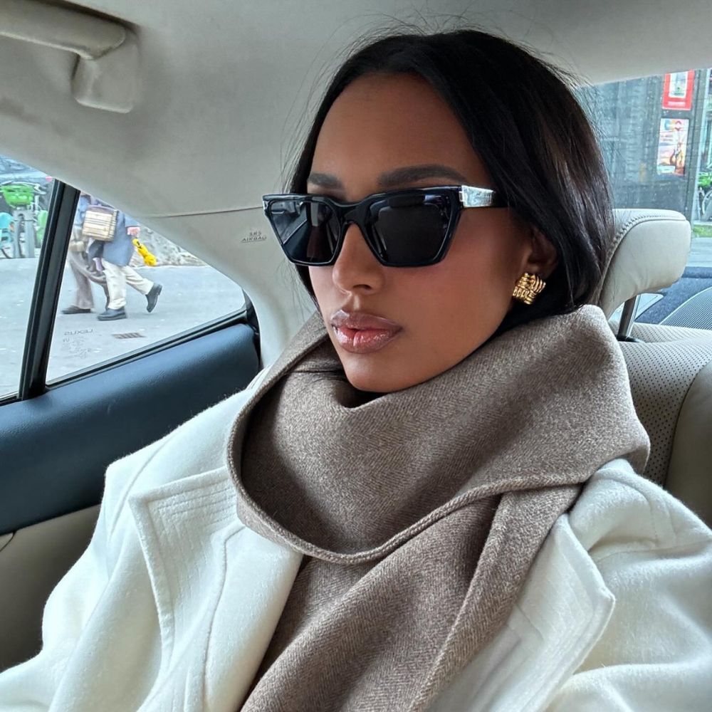 Jasmine Tookes in the back of a car wearing sunglasses and a chic white coat