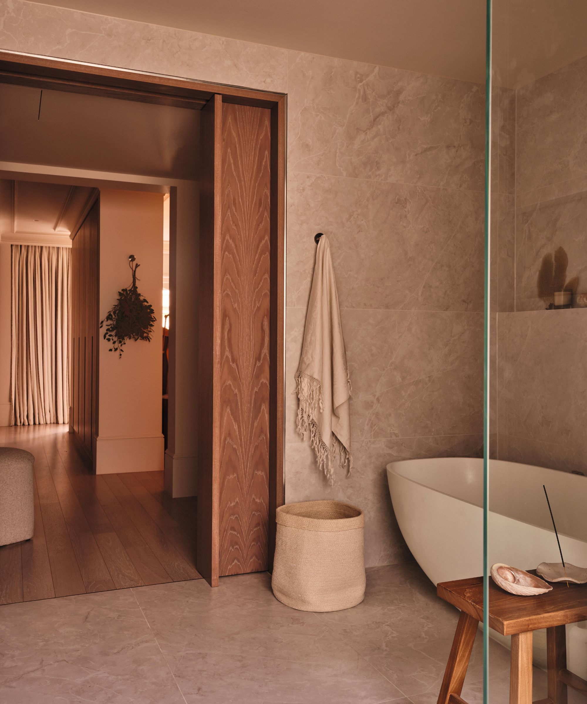 a large neutral bathroom with a sliding wooden door, modern freestanding tub and floor to ceiling stone tiles