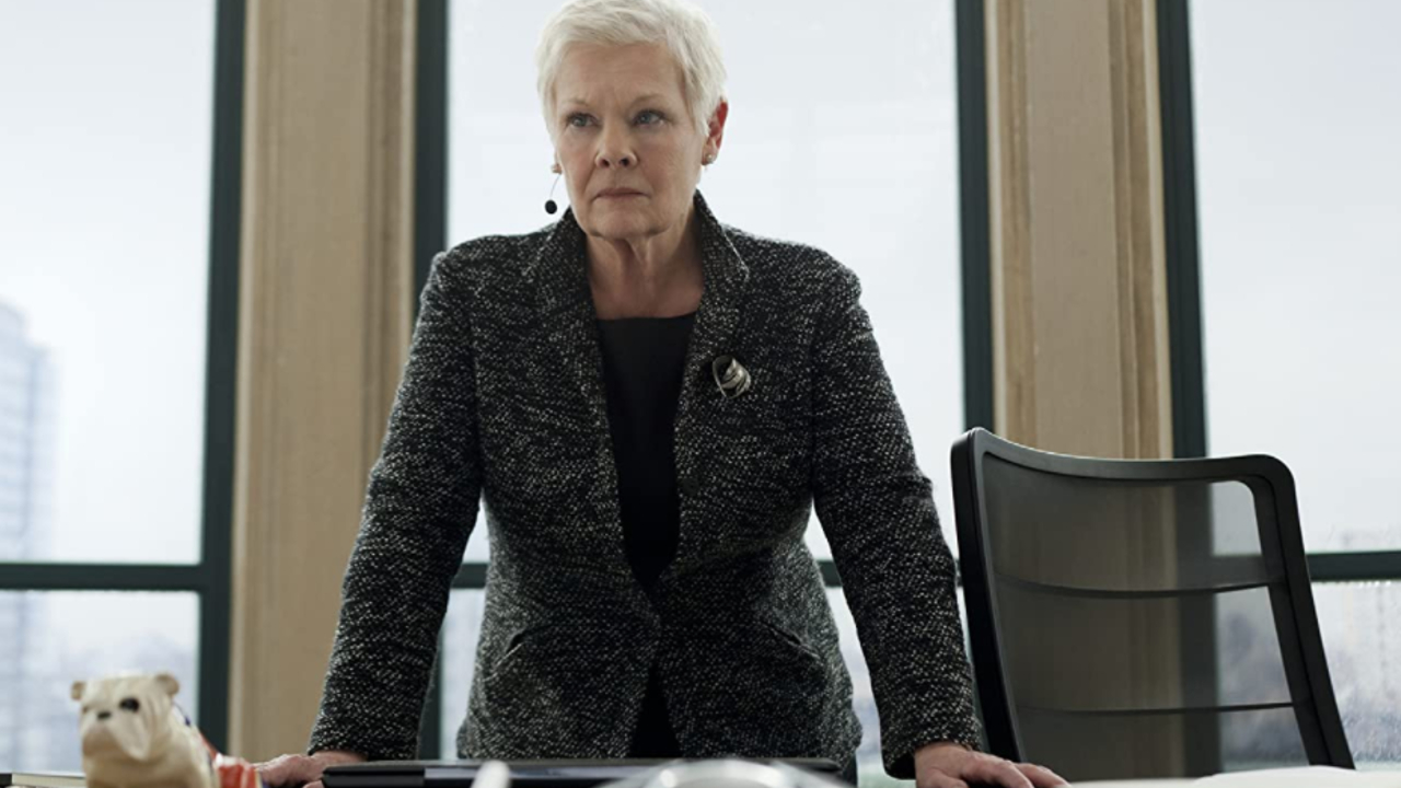 Dame Judi Dench standing at her desk, with Jack the Bulldog in Skyfall.