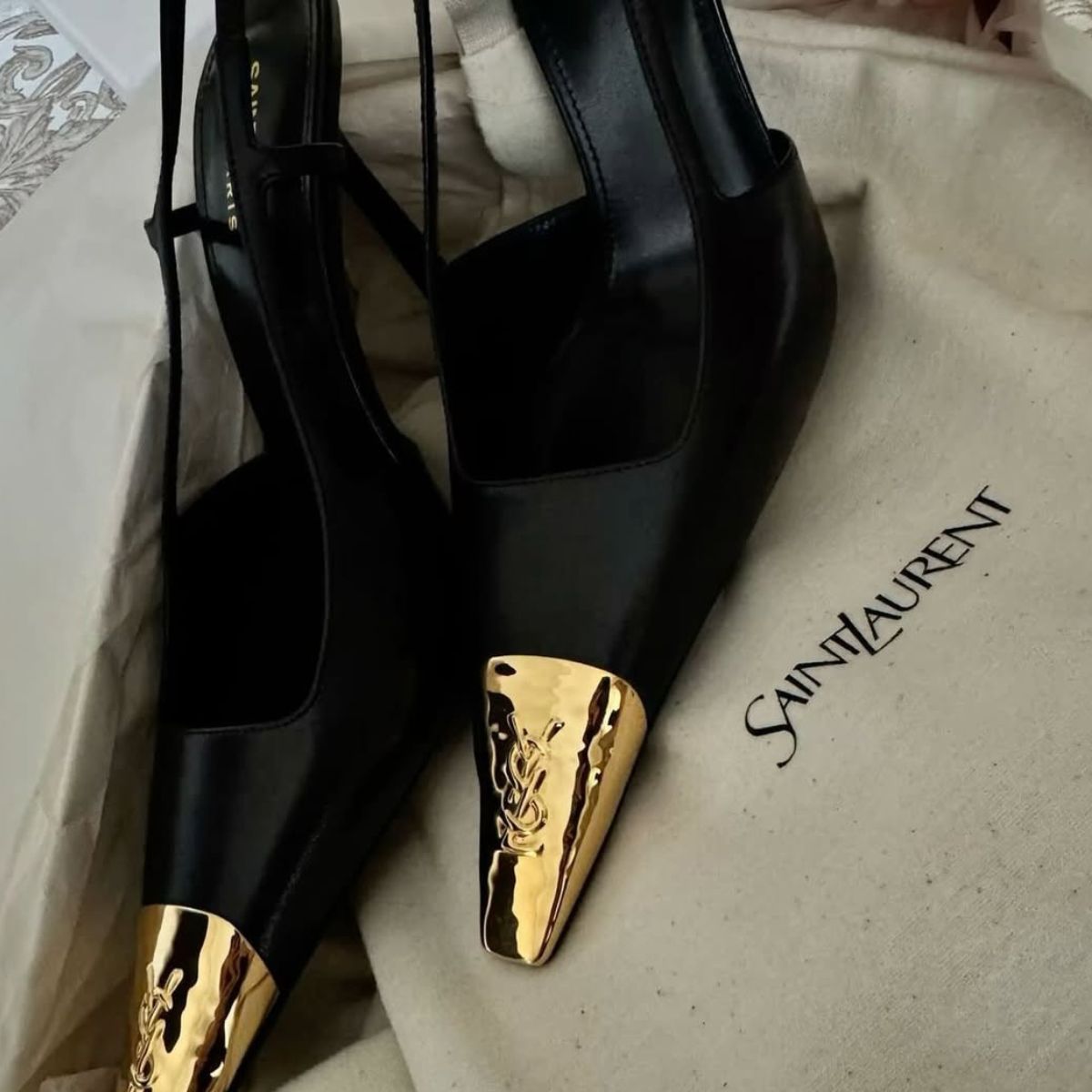 A still life of Saint Laurent Jeanne slingback pumps with gold toes.