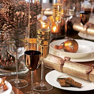 christmas table laid with plates, gold sparkly cracker and glass jars filled with pine cones