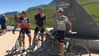 Three white men in cycling attire stand at the top of a mountain road
