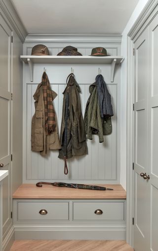 Wooden storage bench in sage mudroom with coat hangers and shelf for hats