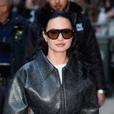 Demi Lovato wearing a belted leather jacket, white skirt, and black sandals
