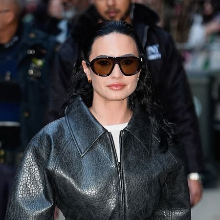 Demi Lovato wearing a belted leather jacket, white skirt, and black sandals