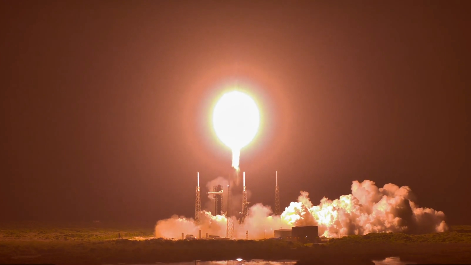 rocket lifting off, there is a bright point of light and plumes along the ground.