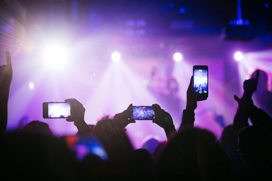 Several people are using their mobile phones to film a live concert.