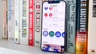 How to set up My Sports on iPhone's News App in iOS 16 promo image of iPhone on shelf showing My Sports