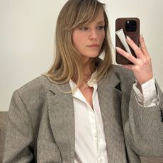 A woman with a bouncy blowdry and fringe taking a mirror selfie with a Rhode phone case