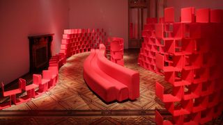 Cherry-coloured modular Élysée shelving, cleaved in two by a snaking Osaka sofa designed by Pierre Paulin