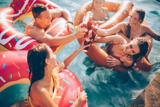 Friends celebrating summer in a pool with bottled beverages