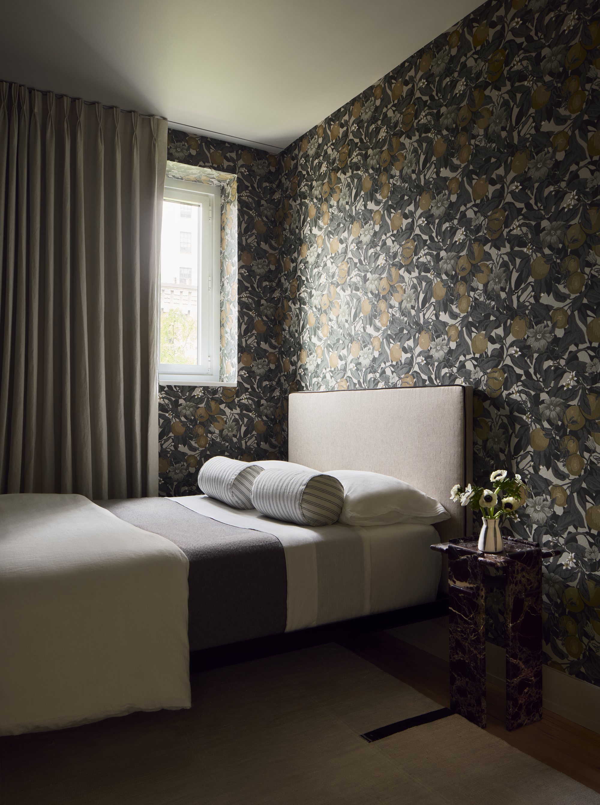 modern bedroom with floral wallpaper, simple bed with bolster pillows, floor-to-ceiling wallpaper