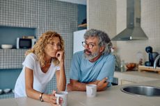 Senior couple sharing breakfast in their modern kitchen, discussing their worries and challenges while sipping coffee and tea together.