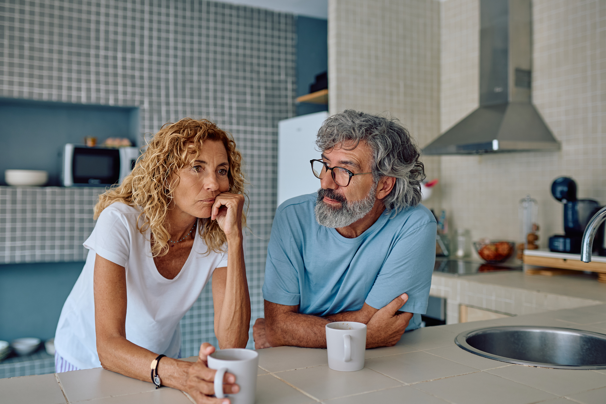 Senior couple sharing breakfast in their modern kitchen, discussing their worries and challenges while sipping coffee and tea together.