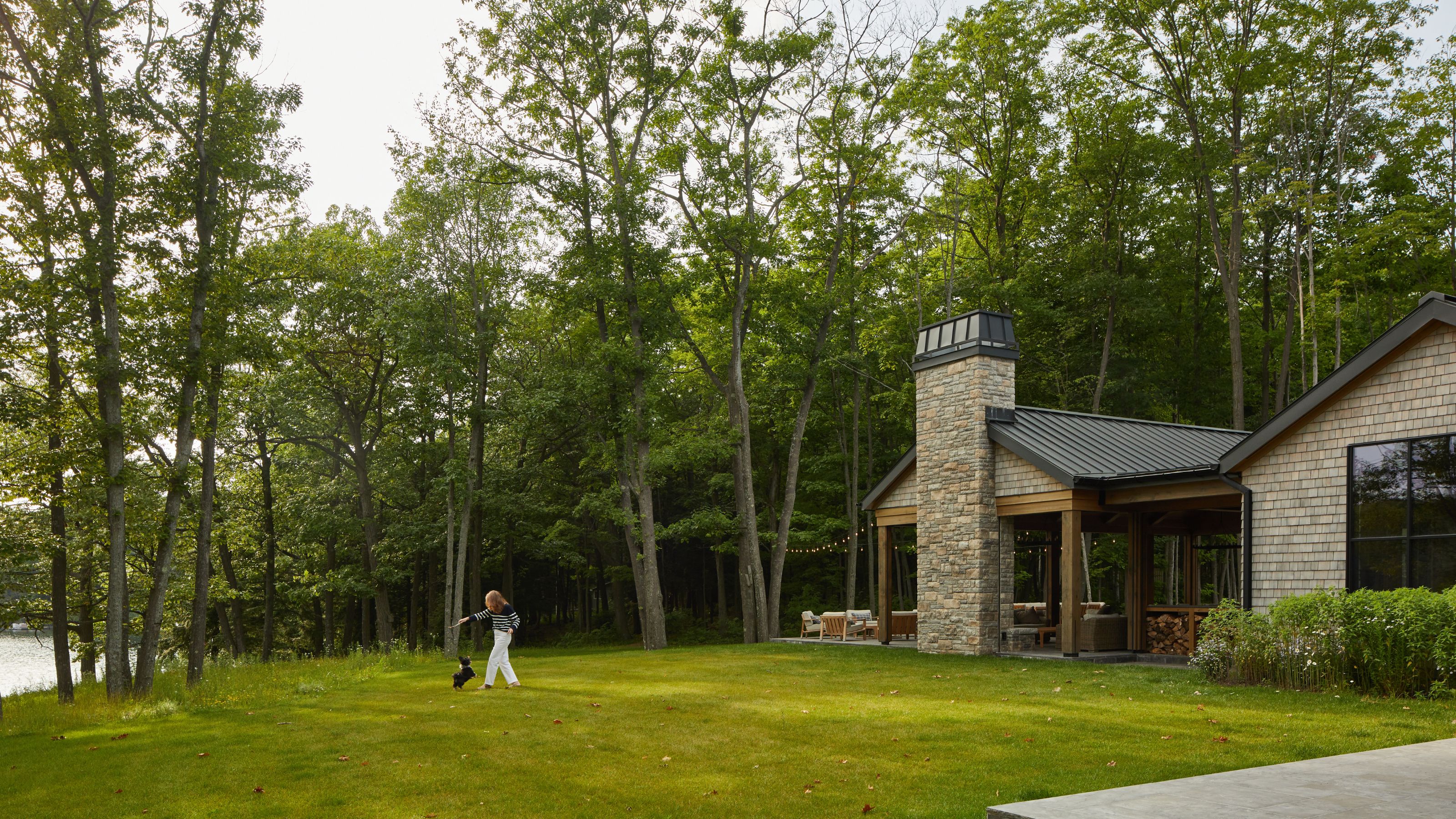 An outdoor living area featuring a large, rustic fieldstone chimney and a covered patio overlooking the lawn.