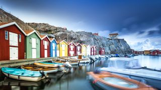 Colorful boathouses by the water with blurred boats in the foreground and rocky cliffs behind