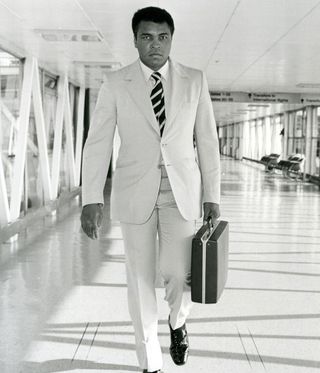 black and white photo of moahmmed ali in a suit holding a briefcase