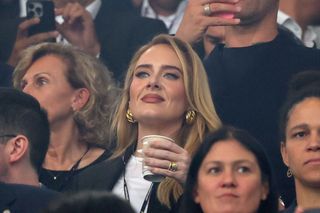 Adele at a soccer game in July 2024 wearing the 80s oversize earrings trend and a white t shirt