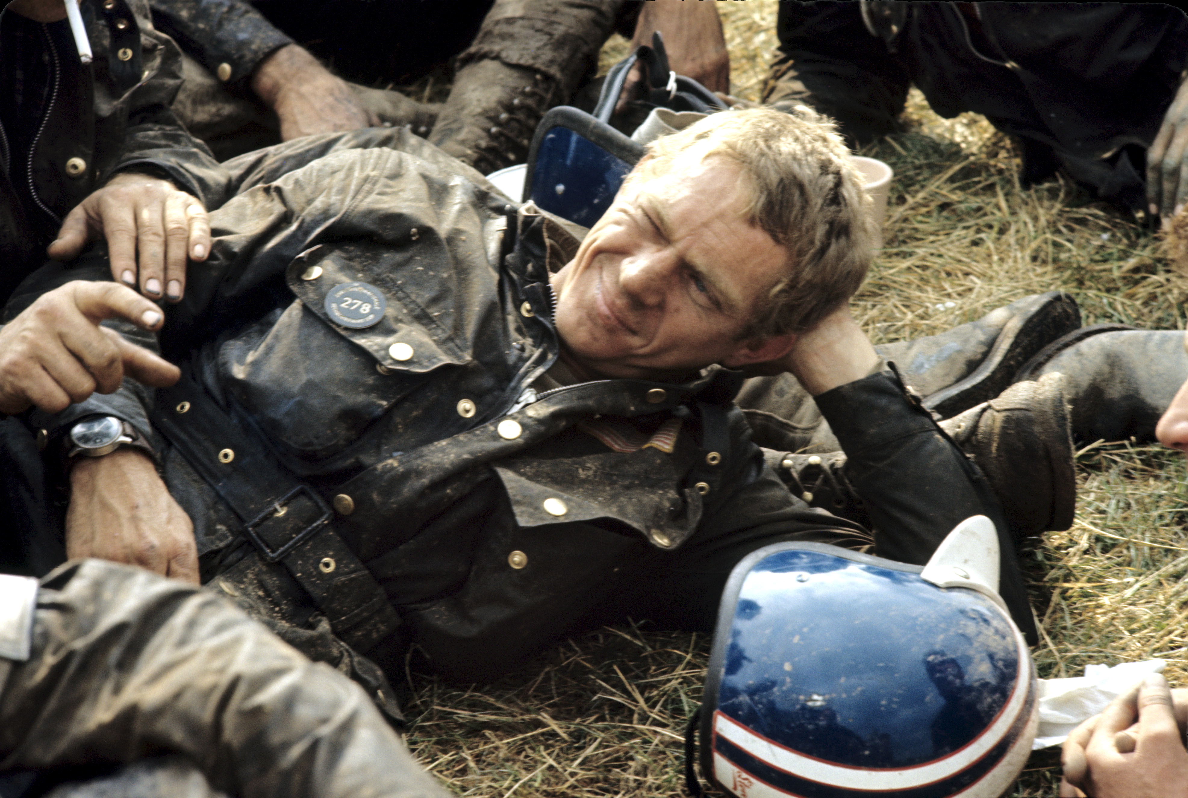Steve McQueen in a wax jacket reclining on the grass 