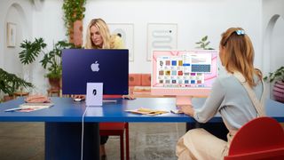 Två kvinnor som sitter i ett vardagsrum och använder en varsin iMac.