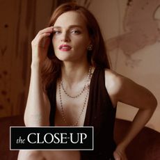 Madeline Brewer sits in a chair wearing a draped pearl necklace with a low cut cong tri gown