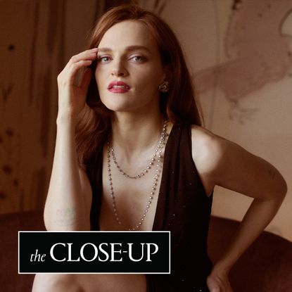 Madeline Brewer sits in a chair wearing a draped pearl necklace with a low cut cong tri gown