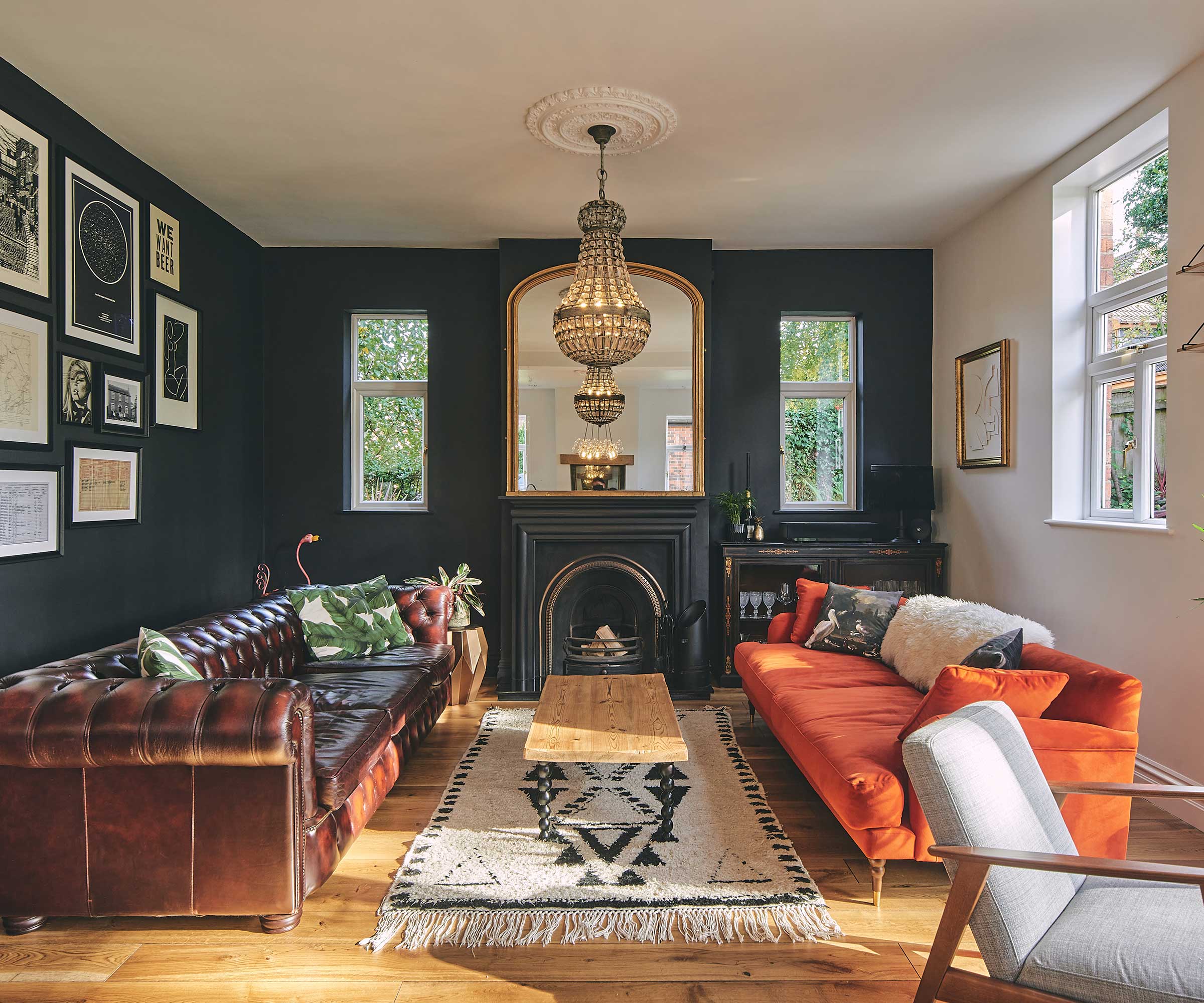 living room with period fireplace, navy painted walls, orange sofa, brown leather sofa and a period-style chandelier