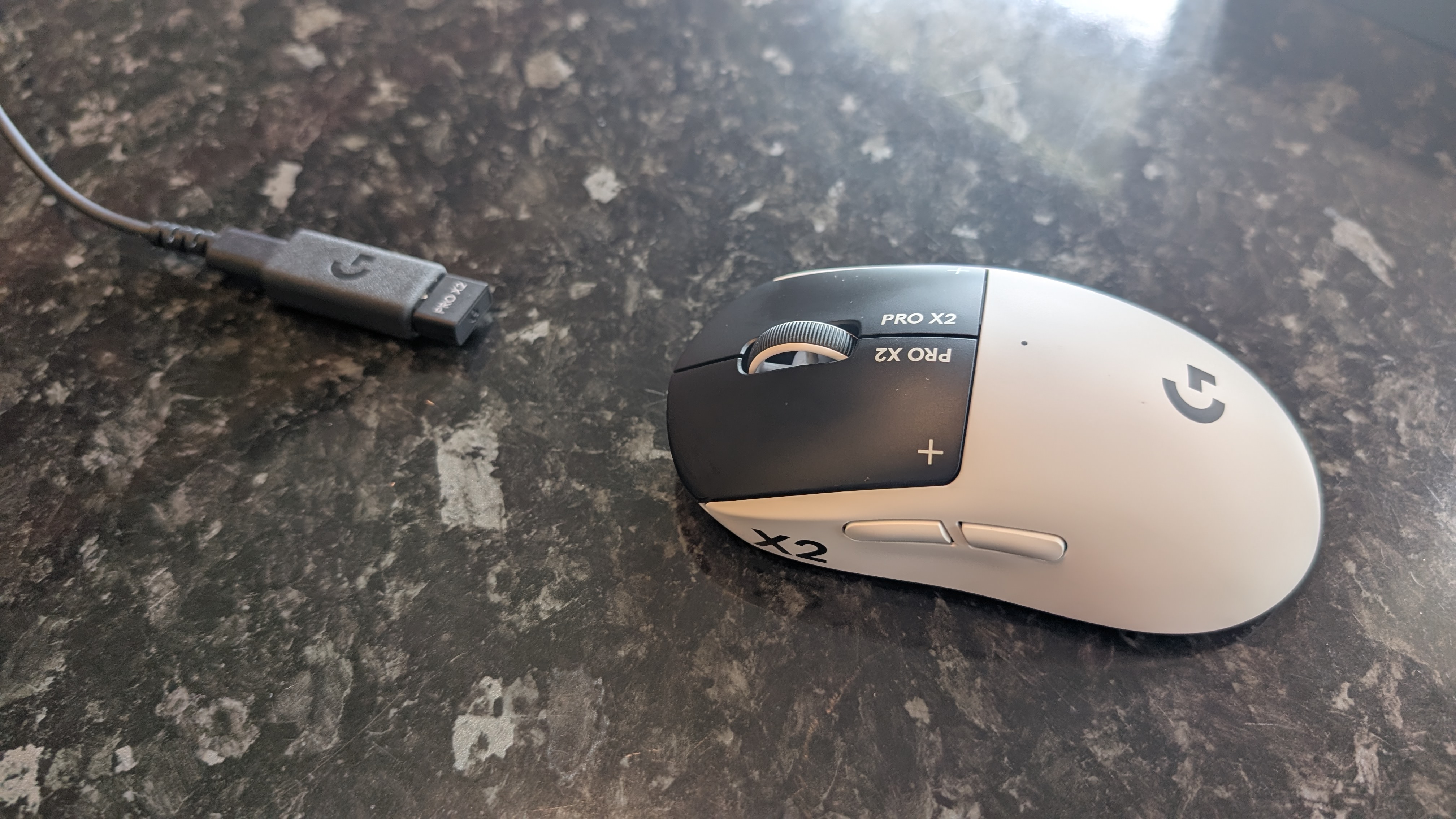 The Logitech G Pro X2 Superstrike pictured on a black marble surface with its wireless adapter.