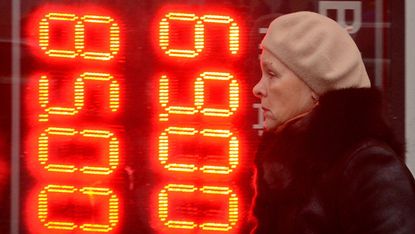 A woman walks past a board listing foreign currency rates outside an exchange office in central Moscow