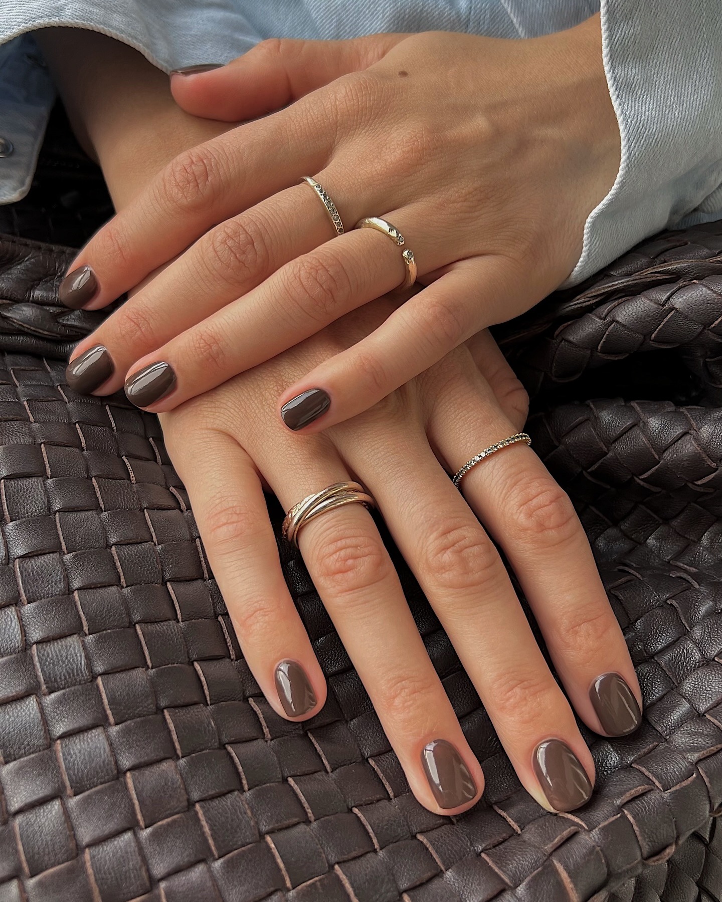 A picture of a woman&#039;s hand on top of a brown woven bag with a brown manicure