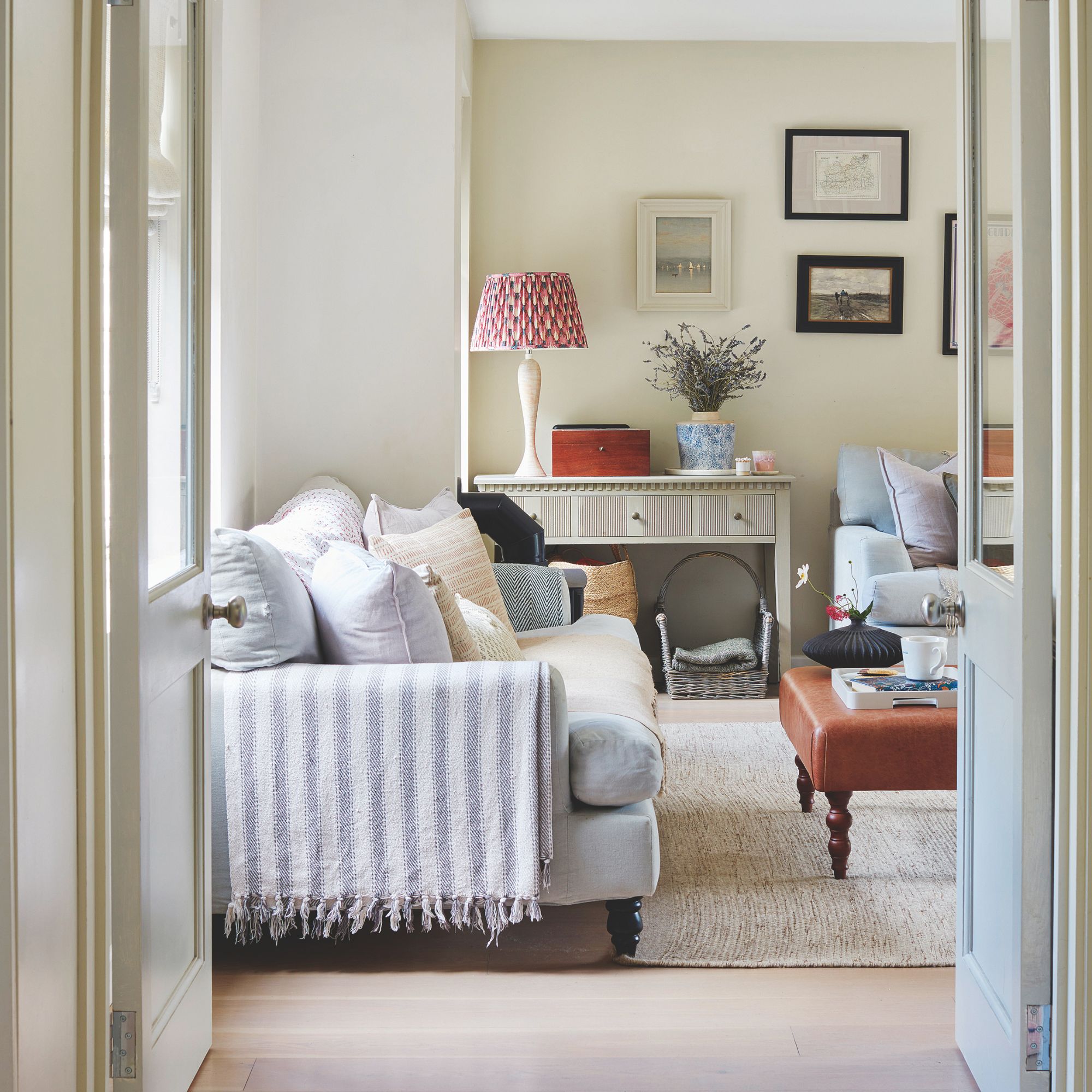 Cream living room with a grey sofa and a console table with a lamp and flowers on it
