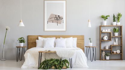 A white bedroom with pair of white pendant ceiling light fixtures, pair of bedside tables and houseplants