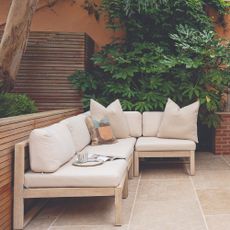 A garden with a minimalist Scandi-style corner sofa in light wood with cream cushions