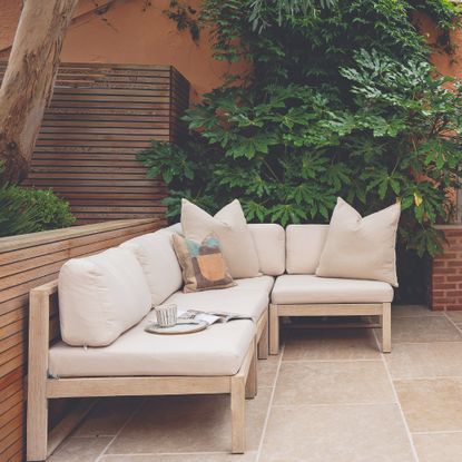 A garden with a minimalist Scandi-style corner sofa in light wood with cream cushions