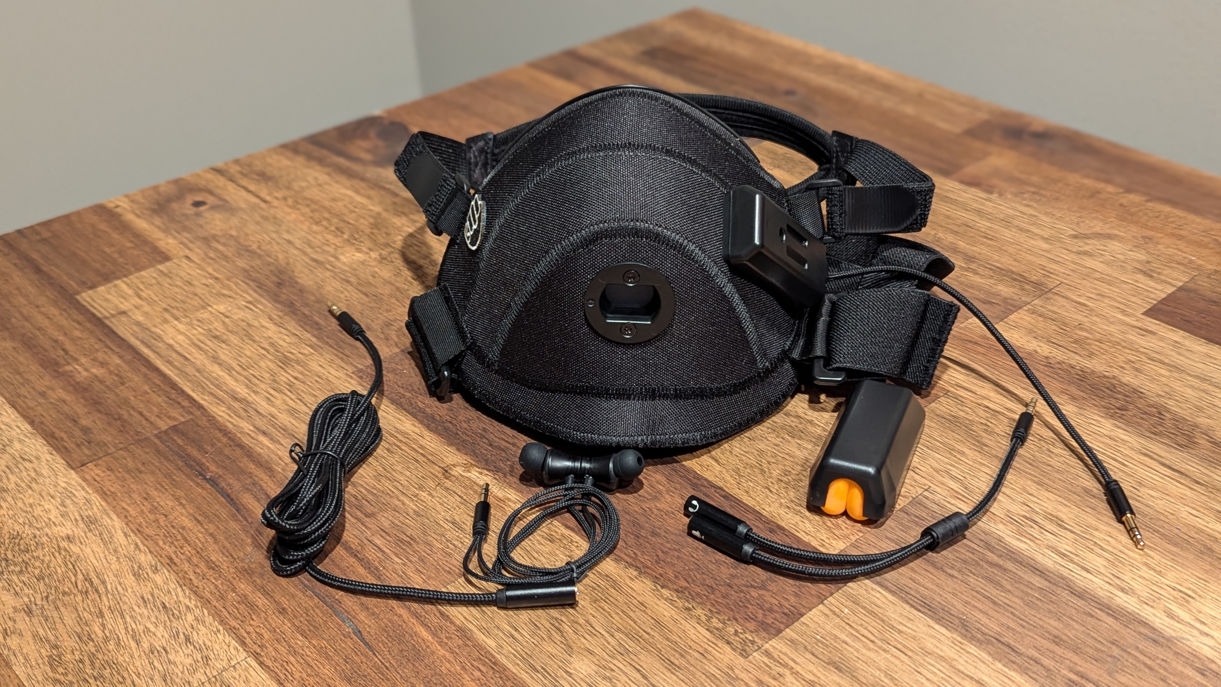 An unpackaged Metadox Ombra mask showing the black mask with straps, audio cables, earbuds, and supplementary microphone enclosure.