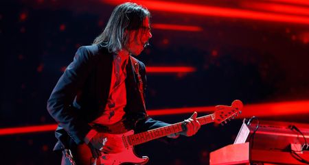 Brian Bell of Weezer plays a Strat with a reverse headstock on a stage lit up in red.