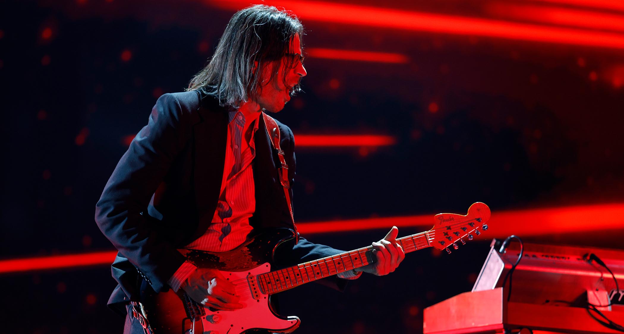 Brian Bell of Weezer plays a Strat with a reverse headstock on a stage lit up in red.