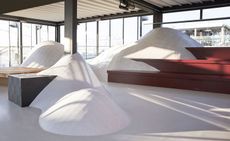 Art display in a floor to ceiling glass room of multiple snow-like hills in different sizes with wood structures attached