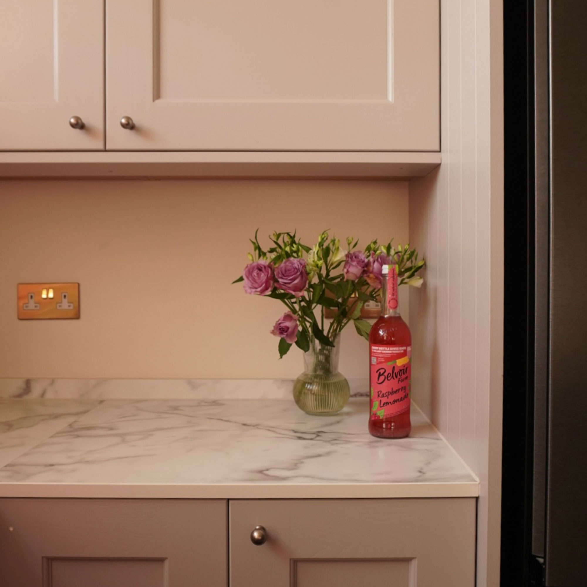 Vase of flowers and bottle of cordial on marble effect worktop in neutral kitchen