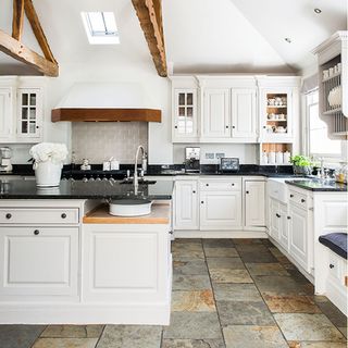 white kitchen with island, ceiling beams and tiled stone flooring