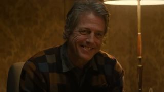 Hugh Grant smiles as he sits in his living room chair in Heretic.