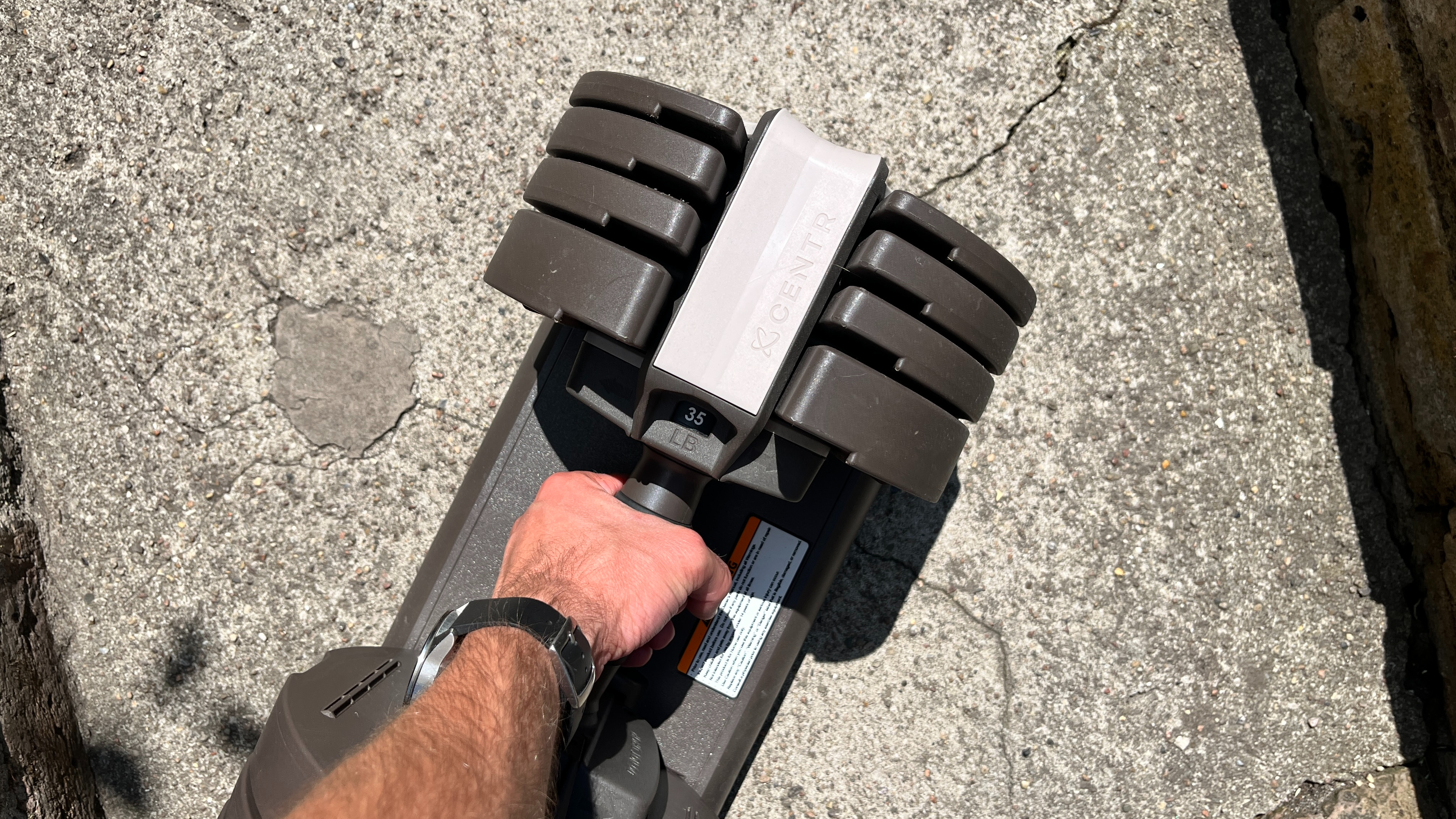 Person about to lift the Centr Smart Stack Adjustable Dumbbell off its storage tray set to 35 lbs