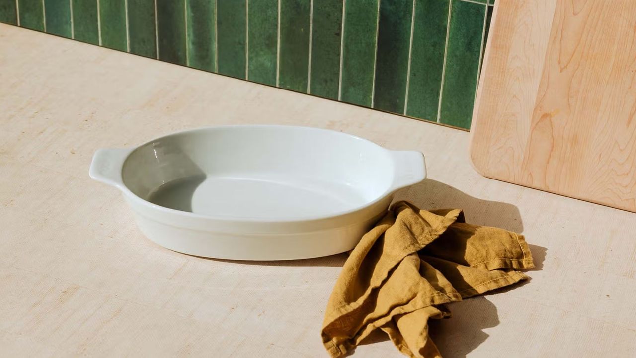 A white porcelain oval baking dish on a wooden kitchen counter, with a green tile back splash
