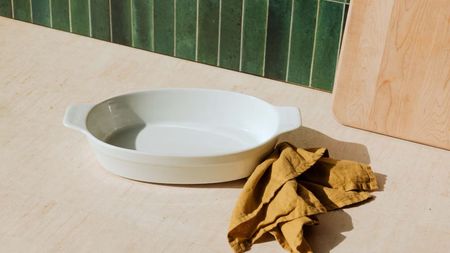A white porcelain oval baking dish on a wooden kitchen counter, with a green tile back splash 