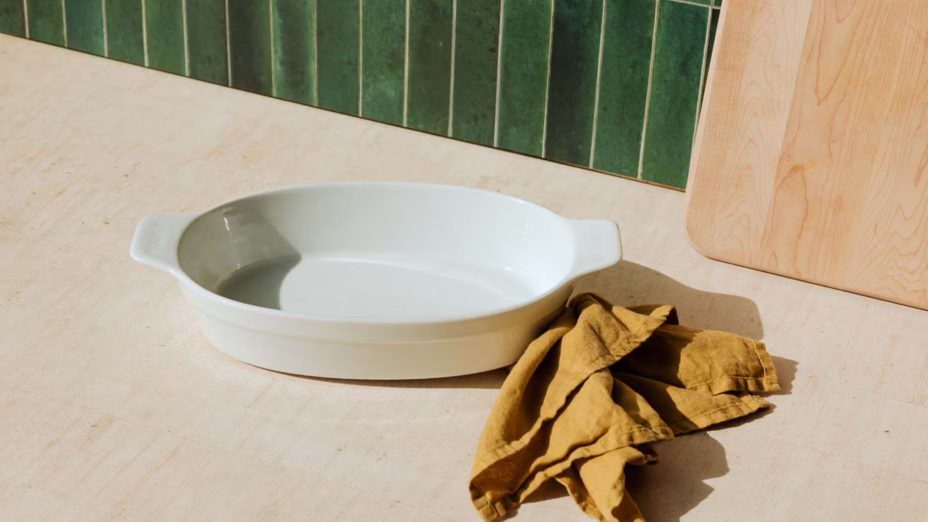 A white porcelain oval baking dish on a wooden kitchen counter, with a green tile back splash 