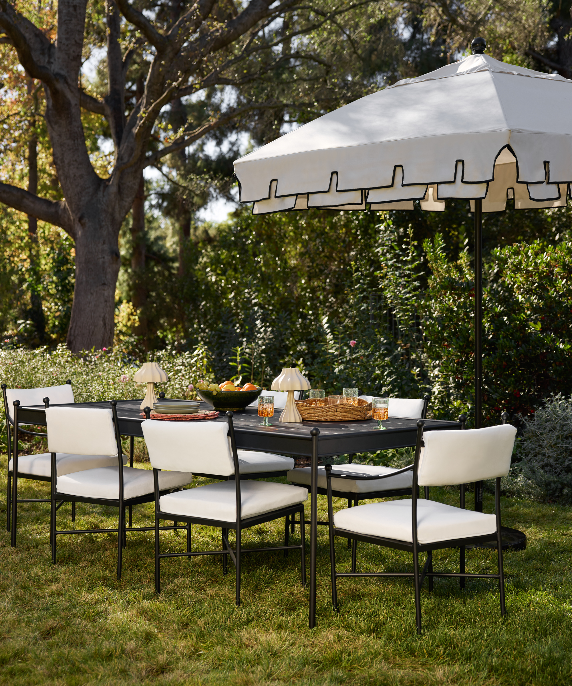 an outdoor dining area with a table, dining chairs with white cushions, and a umbrella