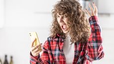 A woman holding her smartphone looks angry and frustrated.