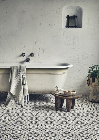 vintage style roll top bath in a rustic bathroom with grey patterned tiles, wooden stool, towel on bath