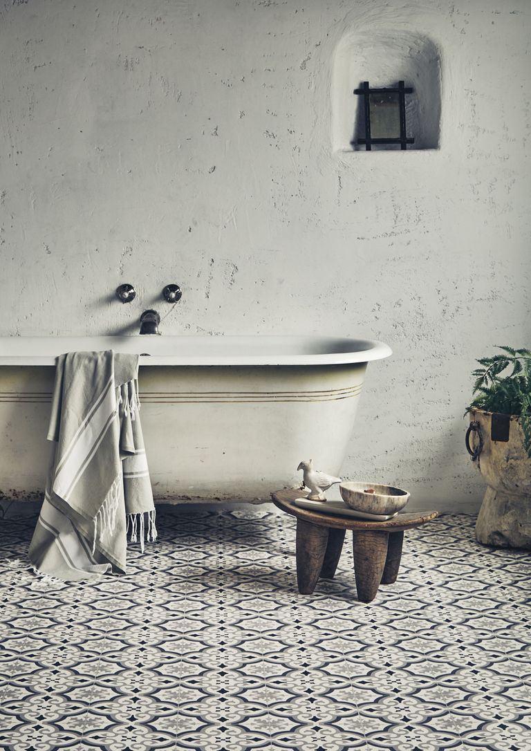 vintage style roll top bath in a rustic bathroom with best bathroom flooring of grey patterned tiles, wooden stool, towel on bath